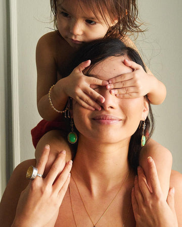 Woman with a child covering her eyes, both wearing green earrings.